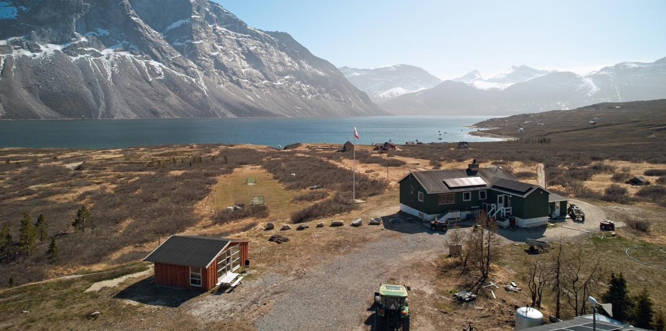 Luftfoto af Qooqqut Nuan ved fjorden, omgivet af høje fjelde