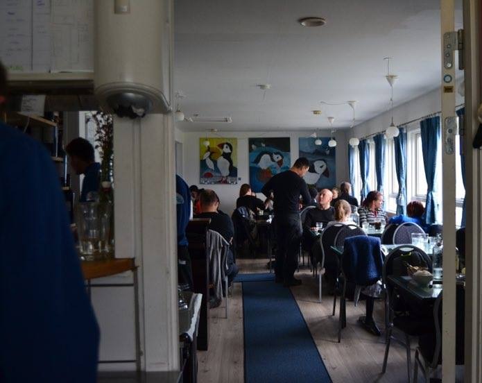 Restaurantens spisesal med gæster ved bordene og malerier af lunder på væggen